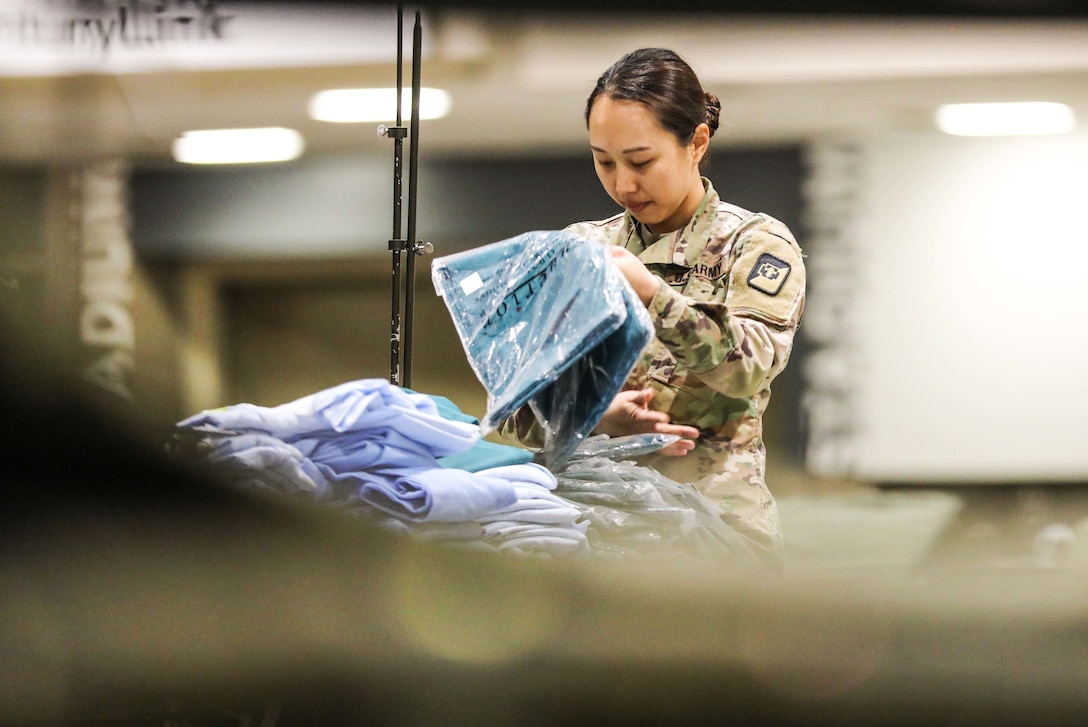 A soldier folds hospital gowns.