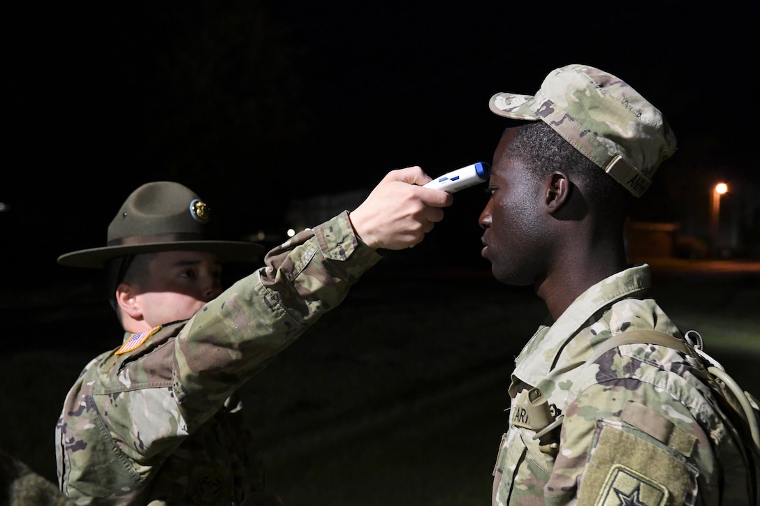 A soldier takes another soldier’s temperature.