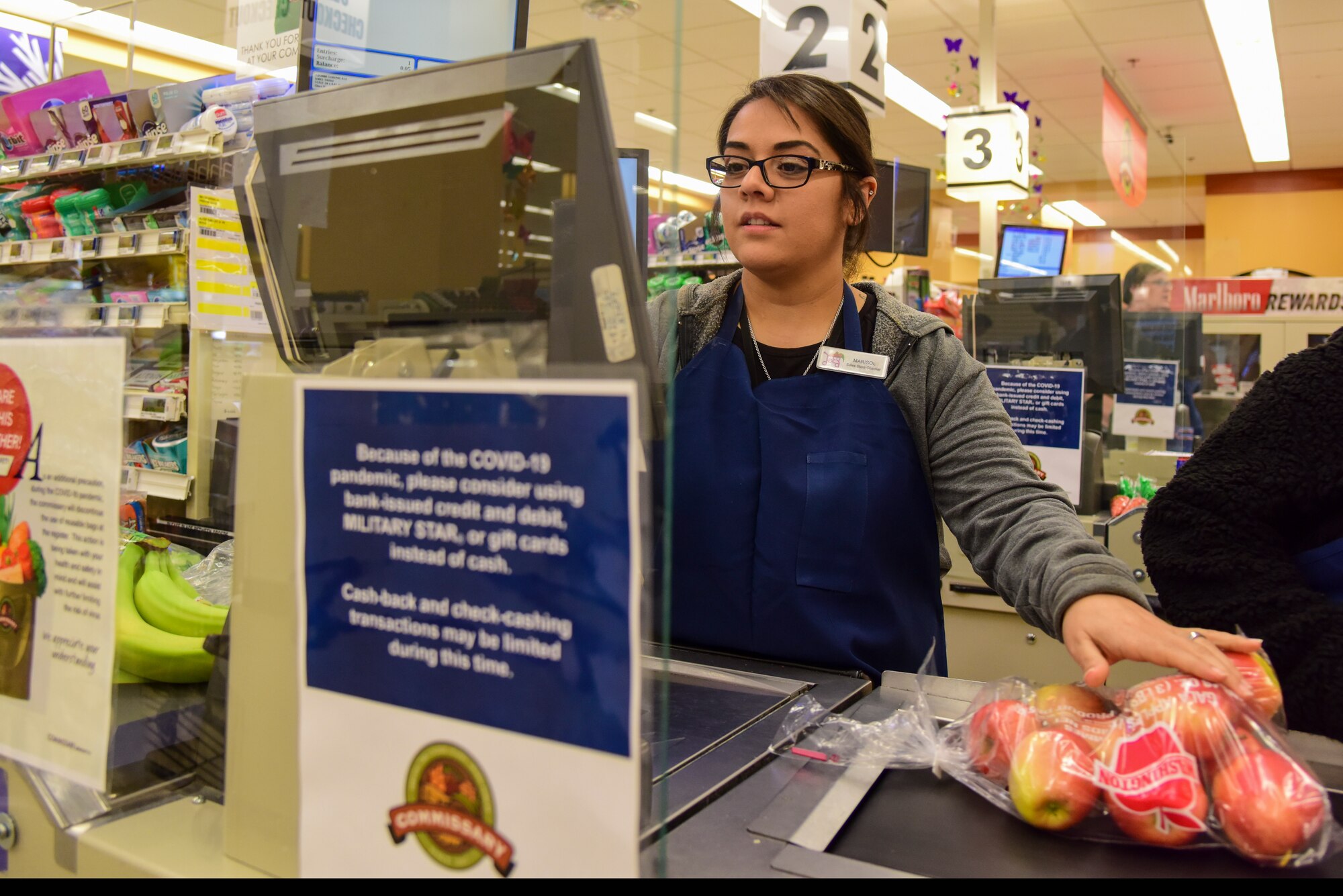 Marisol Cantu, Defense Commissary Agency sales store checker, scans groceries behind a plastic shield to protect the cashiers from germs, March 31, 2020 at Laughlin Air Force Base, Texas. Commissary workers at Laughlin are considered essential personnel during COVID-19 to ensure Airmen here are able to pursue the mission. (U.S. Air Force Photo by Senior Airman Anne McCready)