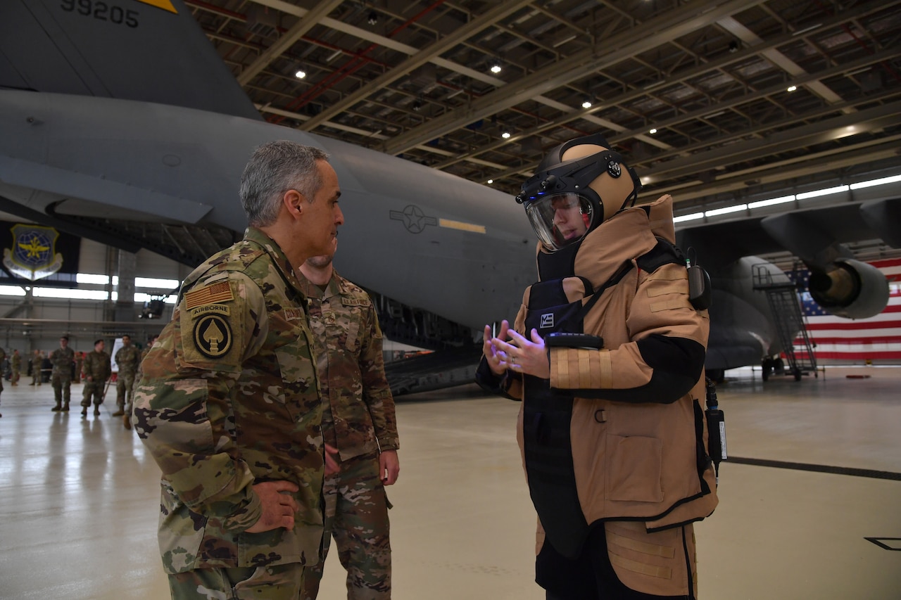A man speaks to an airman wearing a bomb suit.