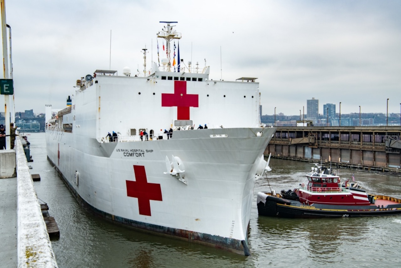 A large white ship with red crosses docks in New York City.