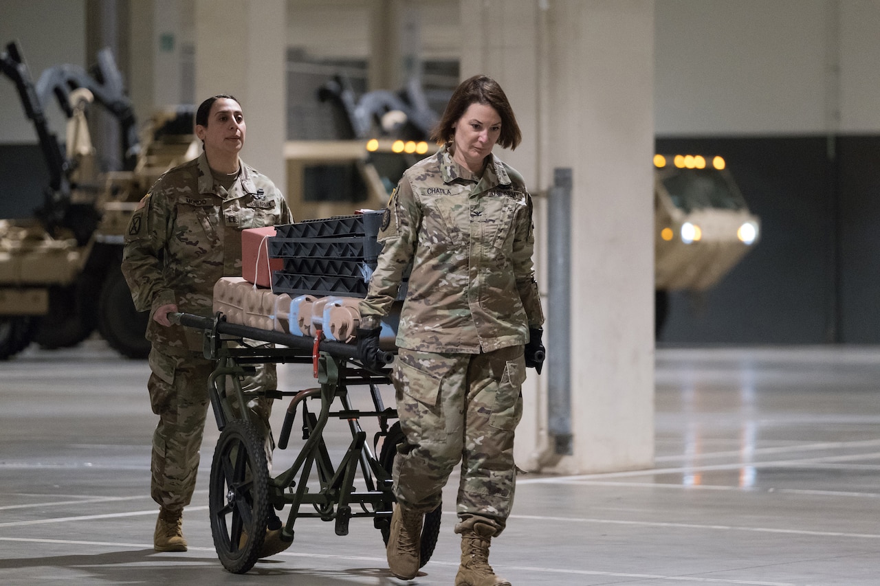Two soldiers use a gurney to move medical supplies.