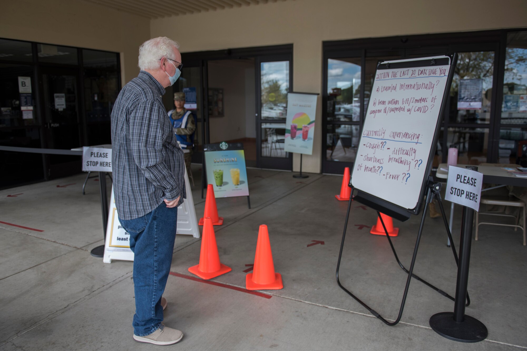 A Base Exchange Satellite Pharmacy customer reads the possible symptoms of COVID-19 outside the Base Exchange Satellite Pharmacy March 30, 2020, at Travis Air Force Base, California. Travis AFB pharmacies implemented multiple procedures to combat COVID-19, including adding a screening at the entrance of the BX Satellite Pharmacy to see if people are experiencing any of the common symptoms of COVID-19. (U.S. Air Force photo by Airman 1st Class Cameron Otte)