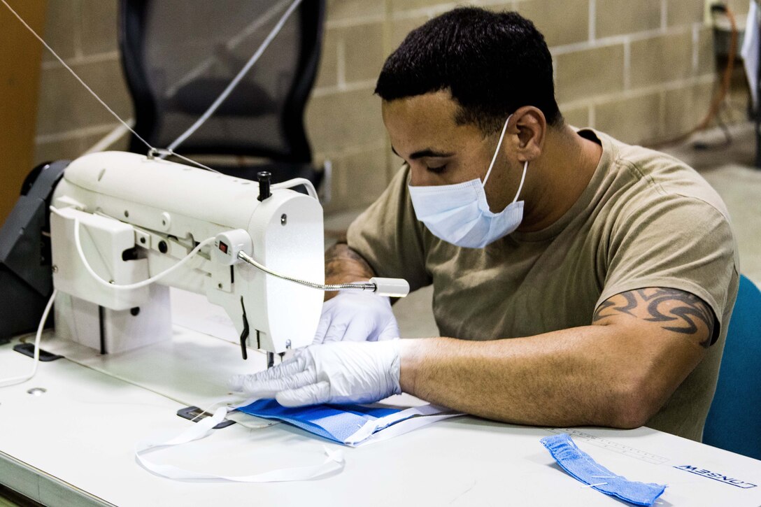 A soldier wearing gloves and a face mask operates a sewing machine.