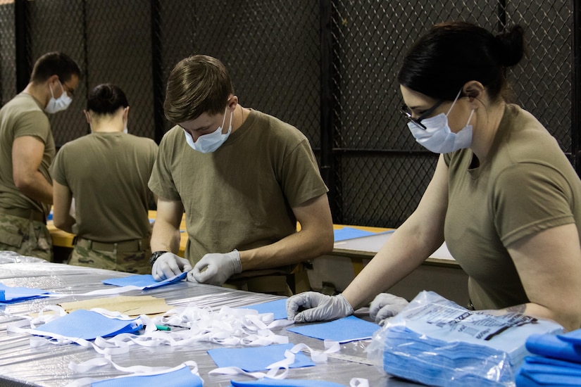 Soldiers wearing gloves and face masks prepare surgical masks for sewing.