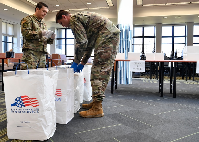Photo of two Airmen packing box lunches in a bag.