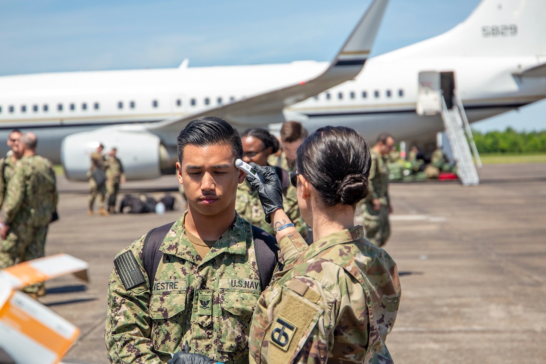 A soldier takes a sailor’s temperature.