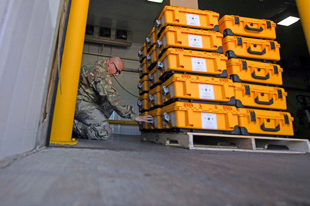 A soldier kneels next to a stack of packages.