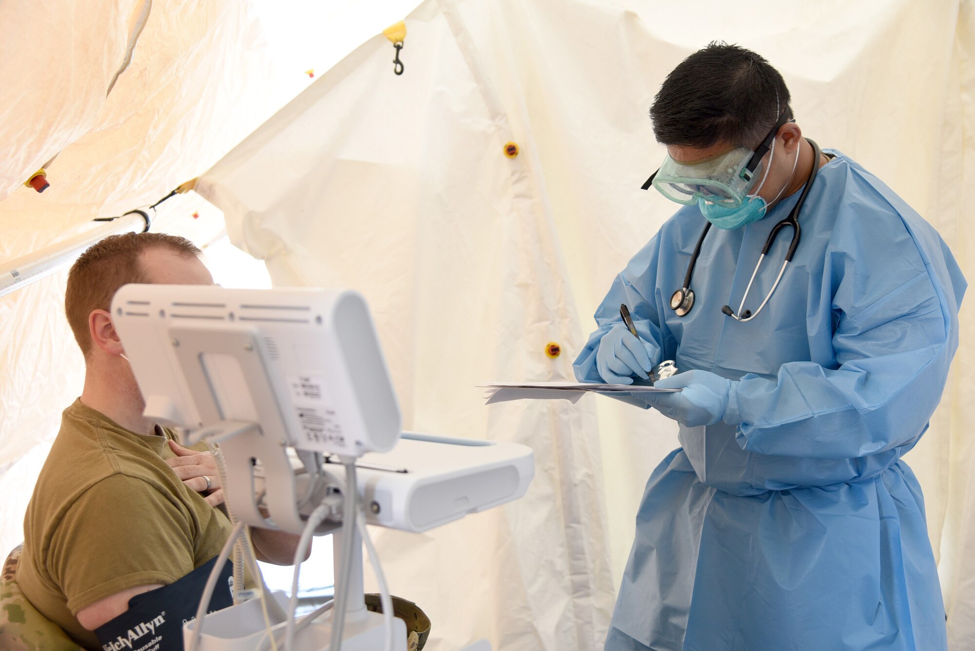 Capt. Audrick Yee writes down information from a patient who had signs of allergies or other upper-respiratory symptoms in the 'sick tent' set up in the front entrance of the 72nd Medical Group clinic. The tent allows medical personnel to provide quicker care to patients without contaminating the inside of the clinic which is currenly being used for patients with scheduled appointments. The patients in the tent are also able to receive any medications they may need while there. Note: the tent is not being used for individuals who may be suspected for COVID-19.