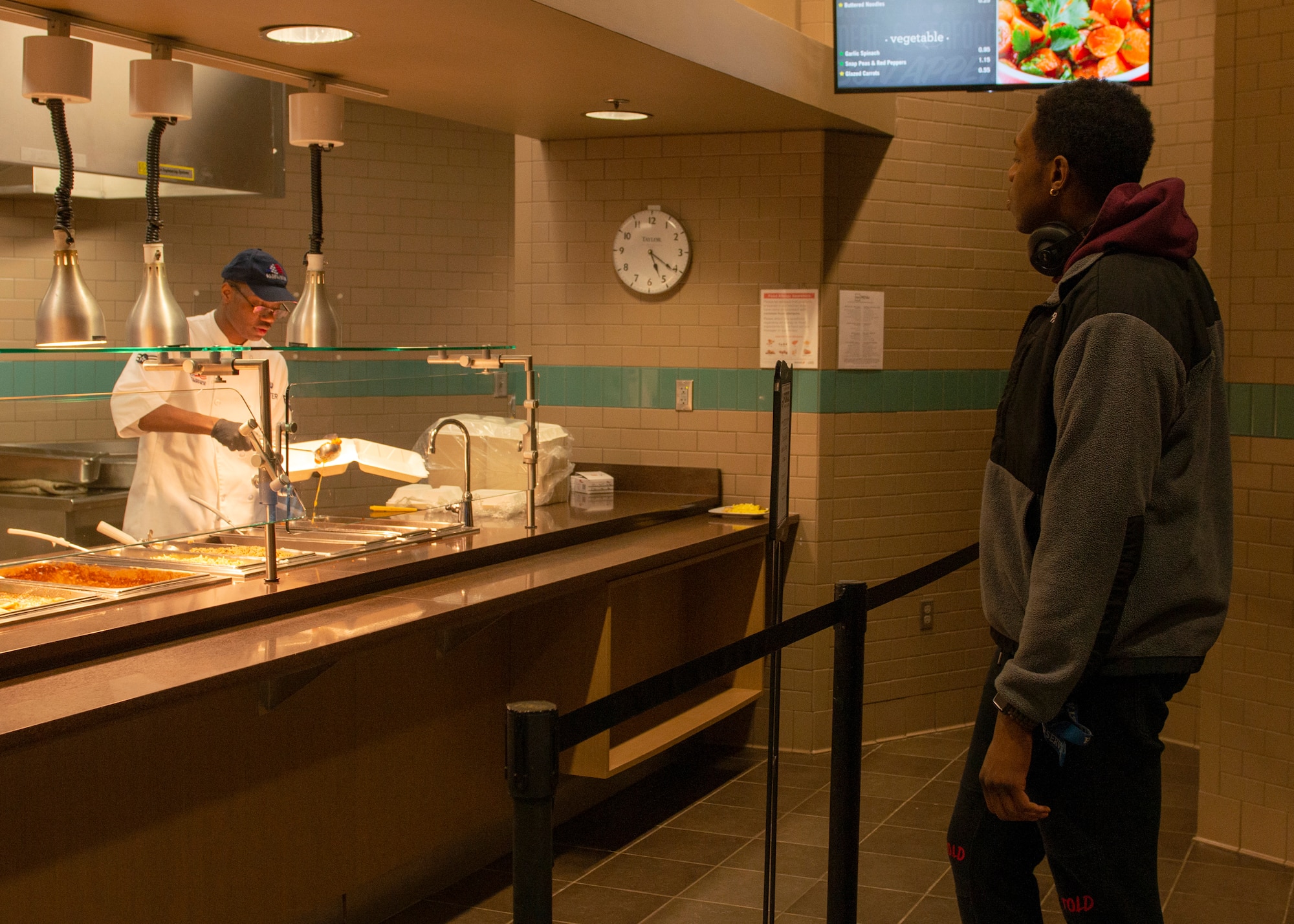 U.S. Air Force Airman 1st Class Robert Shorter, 673d Force Support Squadron food service apprentice, serves U.S. Air Force Airman 1st Class Justin Wynn, 673d Air Base Wing public affairs specialist, in the Iditarod Dining Facility on Joint Base Elmendorf-Richardson, Alaska, April 2, 2020. The dining facility placed boundaries to remind Airmen to stay six feet away from the serving line as a protective measure against COVID-19 while allowing them to support military members to maintain mission readiness.
