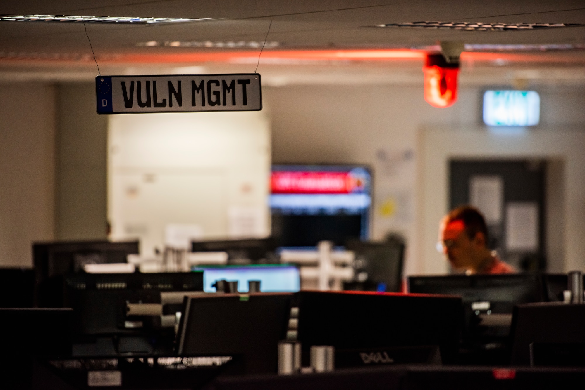 A vulnerability management sign is waning from the ceiling in the middle of a room full of a lot of computers.