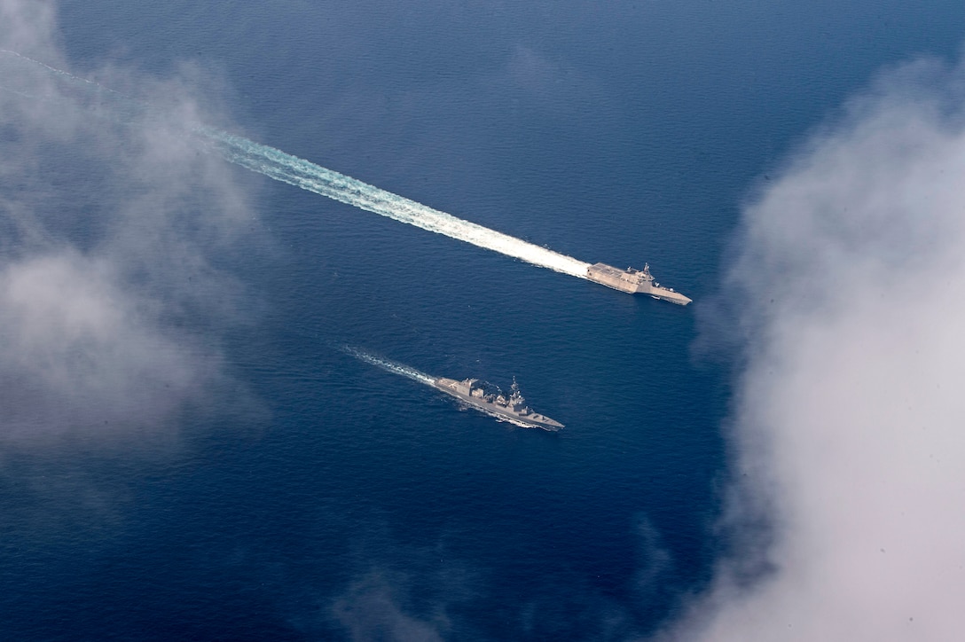 Two ships, seen from overhead, sail side-by-side in blue sea.