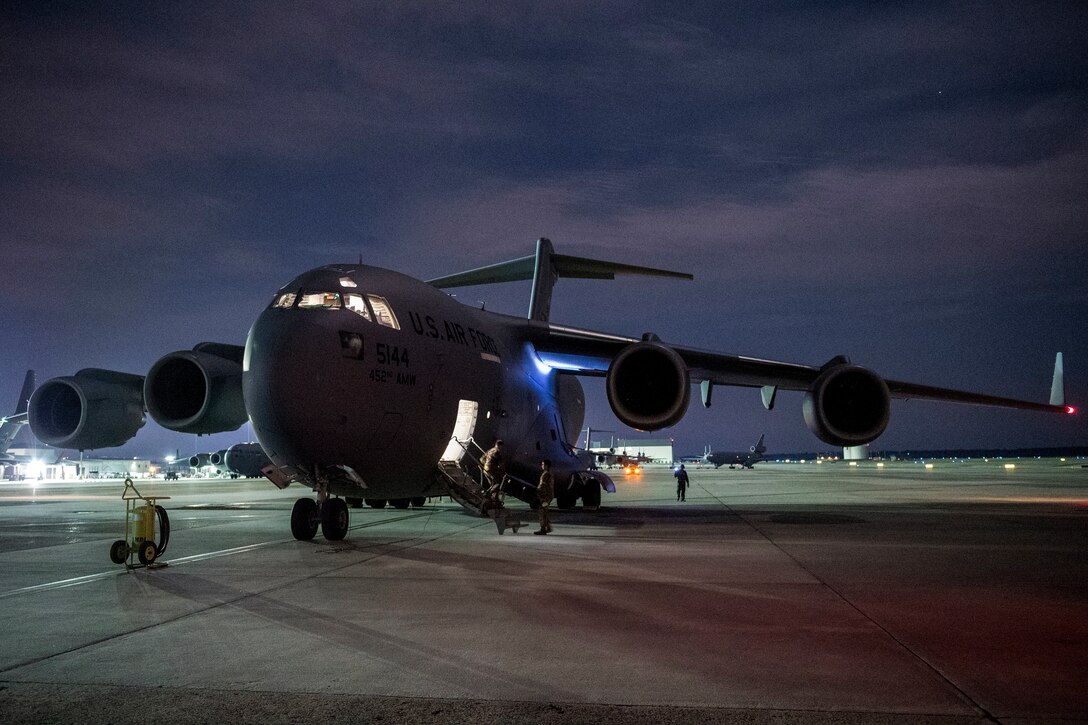 Service members disembark from an aircraft on a flightline against a dark sky.