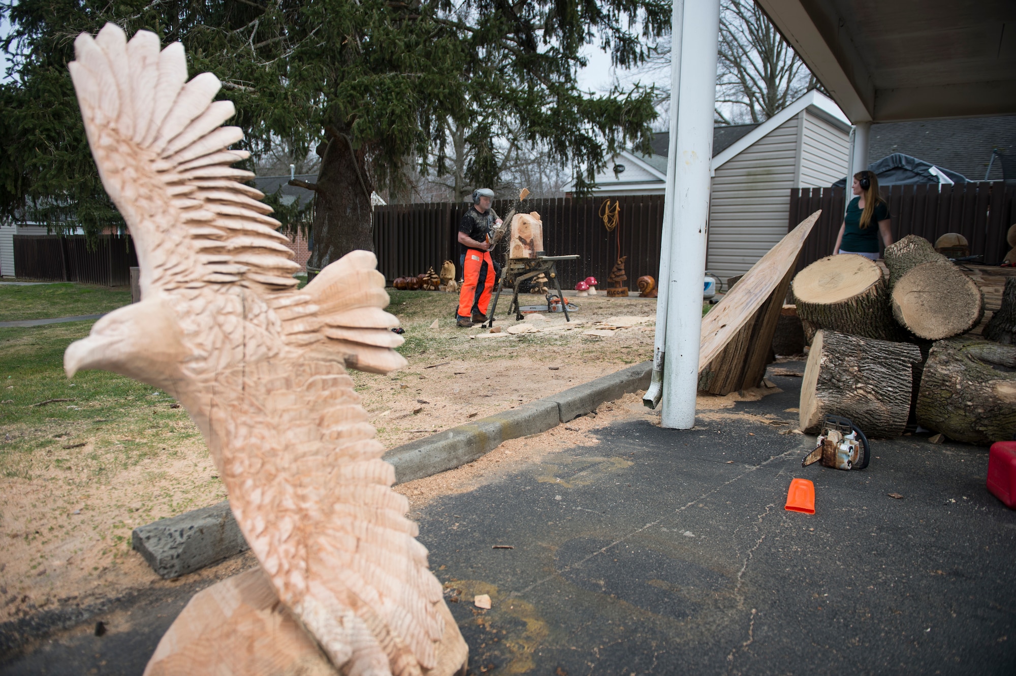 U.S. Air Force Tech. Sgt. Scott Herbert, 818th Mobility Support Advisory Squadron air advisor, begins carving a bear out of wood with a chainsaw as his wife Jennifer watches March 12, 2020, Joint Base McGuire-Dix-Lakehurst, New Jersey. Herbert has three chainsaws to work different cuts and details into his art. (U.S. Air Force photo by Staff Sgt. Sarah Brice)