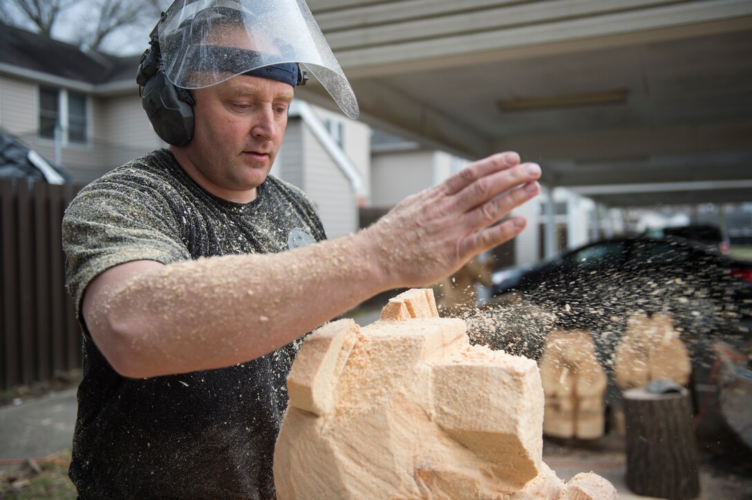 U.S. Air Force Tech. Sgt. Scott Herbert, 818th Mobility Support Advisory Squadron air advisor, dusts off his roughly cut bear carving after using a chainsaw to cut it down to size March 12, 2020, Joint Base McGuire-Dix-Lakehurst, New Jersey. Herbert has three chainsaws to work different cuts and details into his art. (U.S. Air Force photo by Staff Sgt. Sarah Brice)