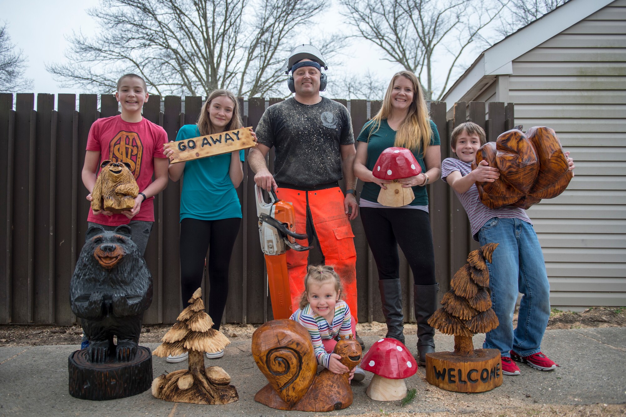 U.S. Air Force Tech. Sgt. Scott Herbert, center, 818th Mobility Support Advisory Squadron air advisor, poses with his family and their favorite carvings that he created with his chainsaw March 12, 2020, Joint Base McGuire-Dix-Lakehurst, New Jersey. Herbert's family chips in to offer support with painting, sanding and blow-torching the sculptures. (U.S. Air Force photo by Staff Sgt. Sarah Brice)