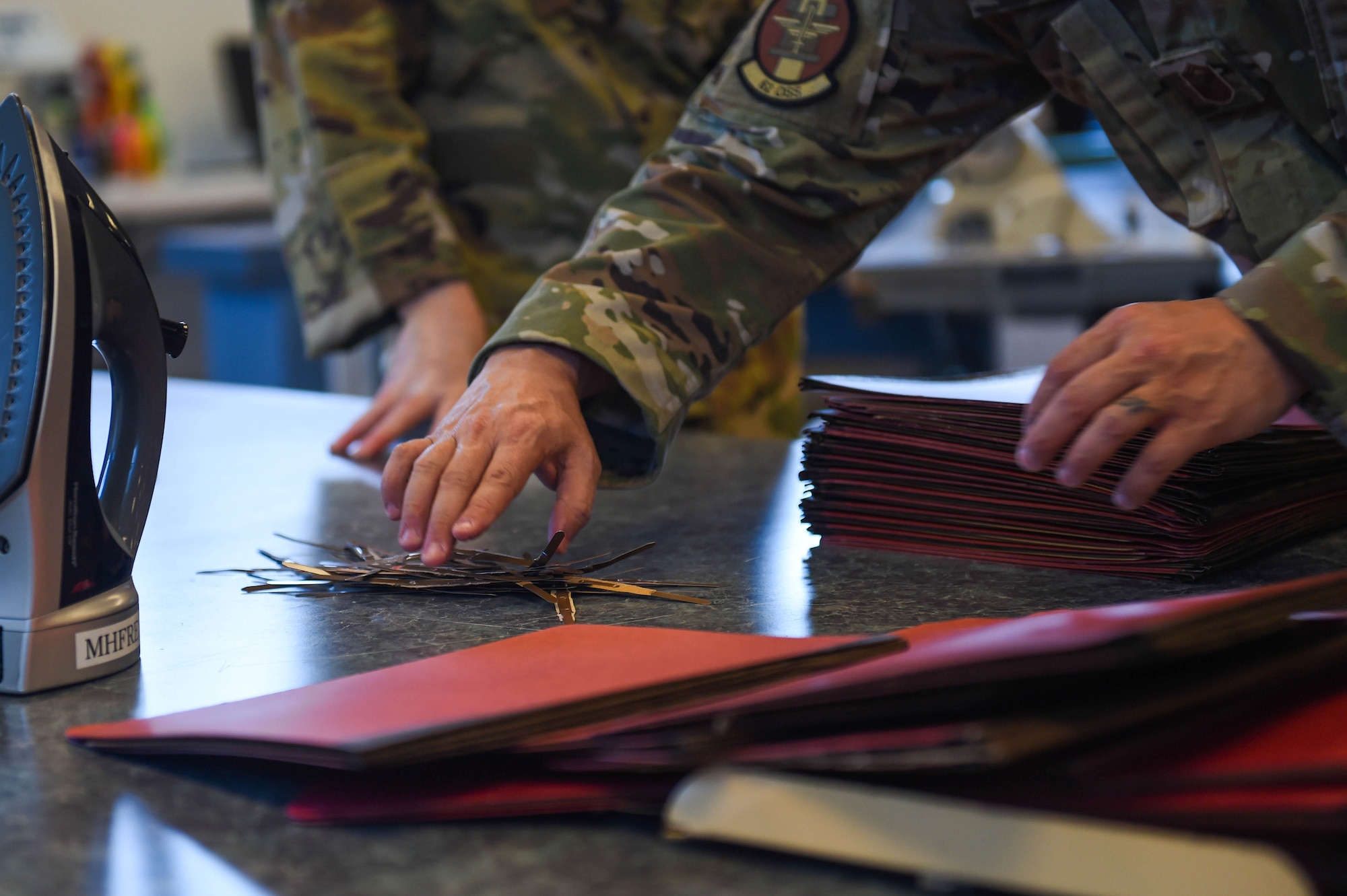 Senior Master Sgt. Samuel Cole, 62nd Operations Support Squadron superintendent, reaches for a pile of metal strips taken from folders to produce cloth face masks at the 62nd OSS aircrew flight equipment fabrication shop on Joint Base Lewis-McChord, Wash., April 6, 2020. The metal strips were sewn into the part of the mask that goes over the nose to make it more form-fitting and create more of a seal. (U.S. Air Force photo by Airman 1st Class Mikayla Heineck)