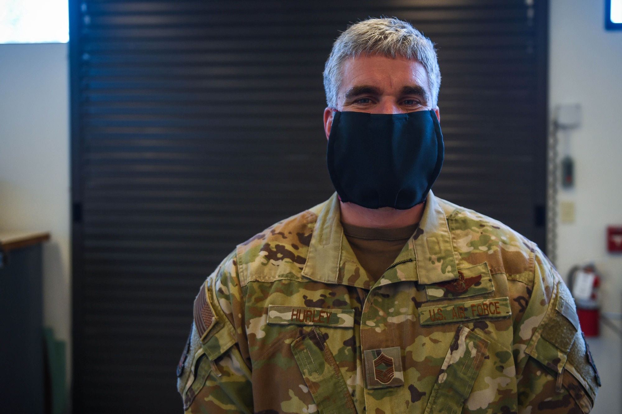 Chief Master Sgt. Skip Hurley, 62nd Operations Group chief enlisted manager, poses with a completed cloth face mask in the 62nd Operations Support squadron aircrew flight equipment fabrication shop on Joint Base Lewis-McChord, Wash., April 6, 2020. Mask production is not what the 62nd OSS AFE fabrication shop normally produces, but the unit innovatively adjusted to the mission requirements due to the COVID-19 outbreak. (U.S. Air Force photo by Airman 1st Class Mikayla Heineck)