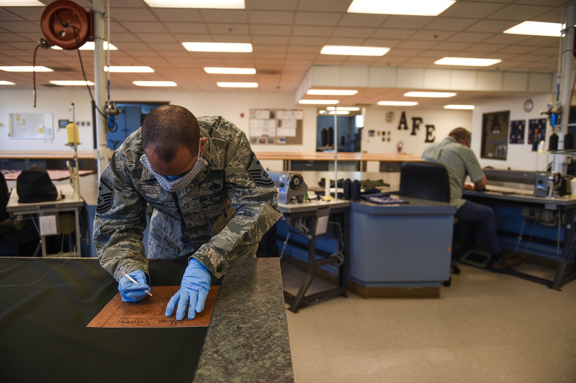 Master Sgt. Yosuel Muniz, 62nd Operations Support Squadron first sergeant, marks where to cut a sheet of fabric to aid in the production of cloth face masks at the 62nd OSS aircrew flight equipment fabrication (AFE) shop on Joint Base Lewis-McChord, Wash., April 6, 2020. The 62nd OSS AFE fabrication shop normally produces the fabric for aircraft seats and parachutes, but adjusted their mission to help prevent the spread of COVID-19. (U.S. Air Force photo by Airman 1st Class Mikayla Heineck)