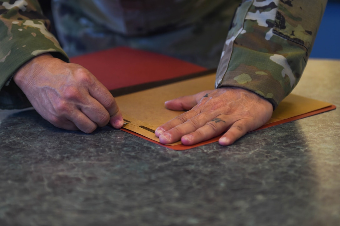 Senior Master Sgt. Samuel Cole, 62nd Operations Support Squadron superintendent, uses a razor to carefully remove the metal strip from a folder to produce cloth face masks at the 62nd OSS aircrew flight equipment fabrication shop on Joint Base Lewis-McChord, Wash., April 6, 2020. The metal strips were sewn into the part of the mask that goes over the nose to make it more form-fitting and create more of a seal. (U.S. Air Force photo by Airman 1st Class Mikayla Heineck)