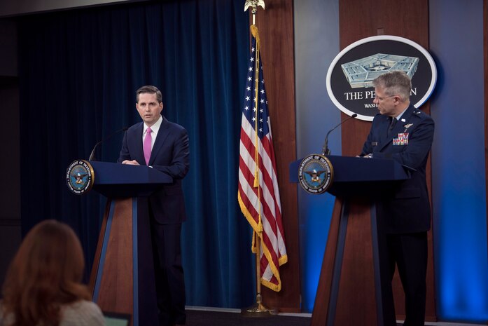 A civilian and an airman stand at lecterns.