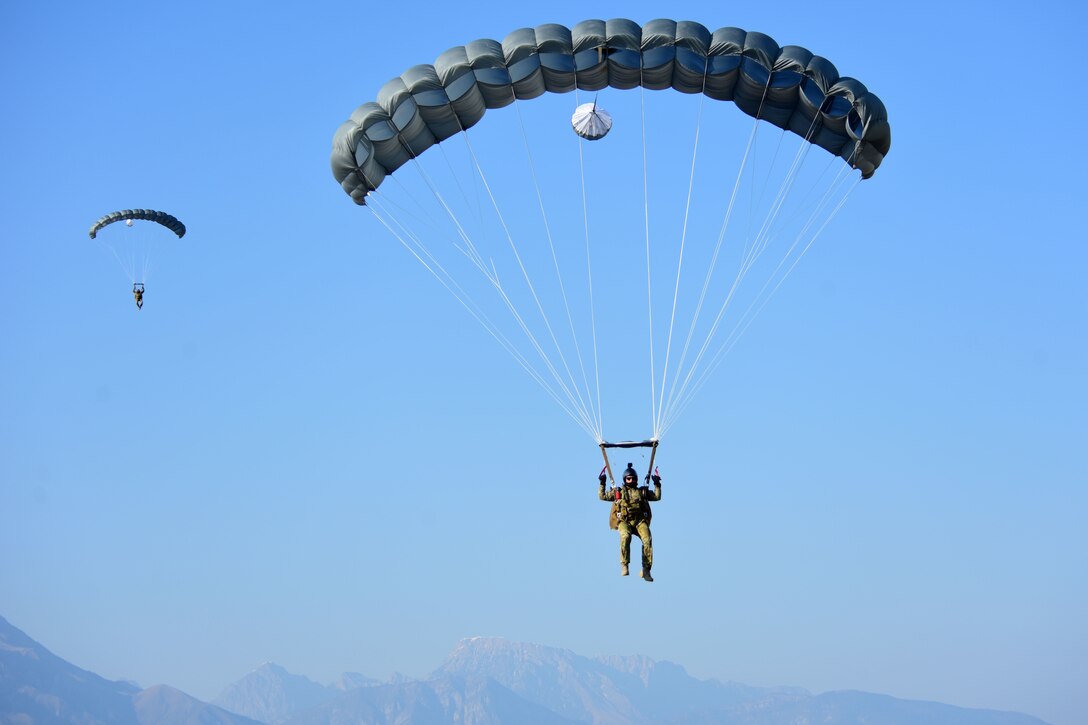 Two airmen parachute to the ground against a blue sky.