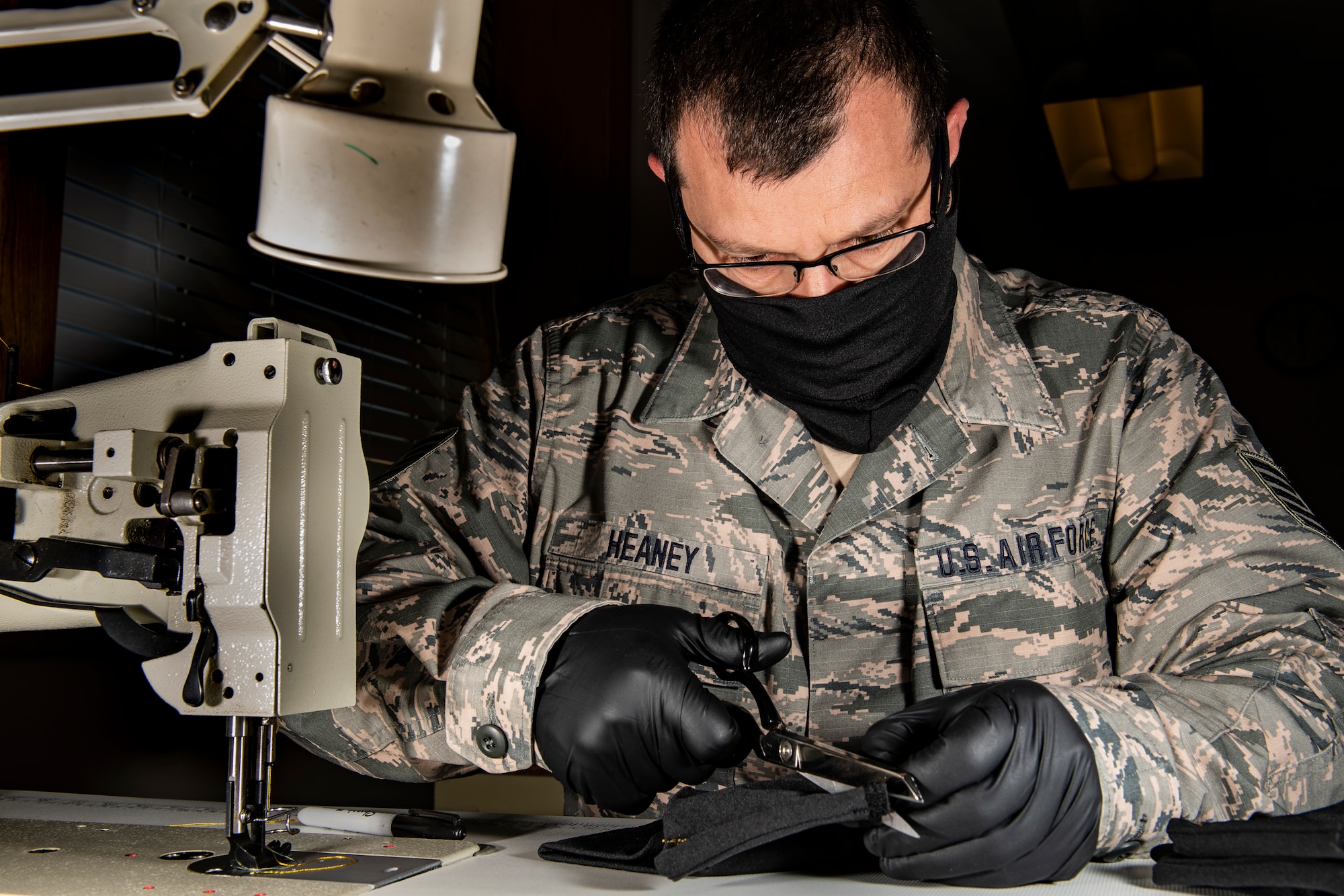 An aircraft flight equipment technician cutting material to make a cloth face mask.
