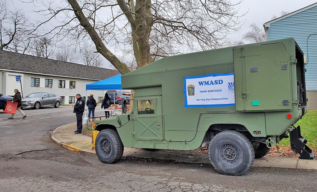 A former military ambulance is parked on a street corner food donation location.