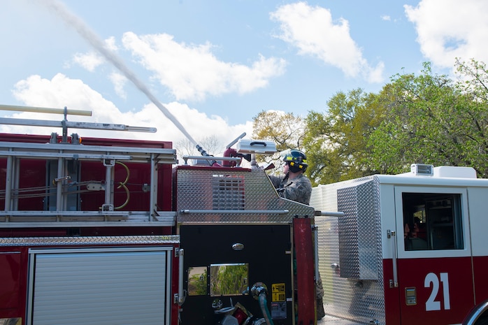 Airman 1st Class Joshua Doms, a firefighter assigned to the 628th Civil Engineering Squadron Department, sprays water from a hose in Hunley Park-Air Base housing on Joint Base Charleston, S.C., March 25, 2020. The Fire Department is still conducting normal operations. Firefighters are taking preventative measures such as cleaning common areas every four hours, and enforcing higher hygiene standards like frequently washing hands.
