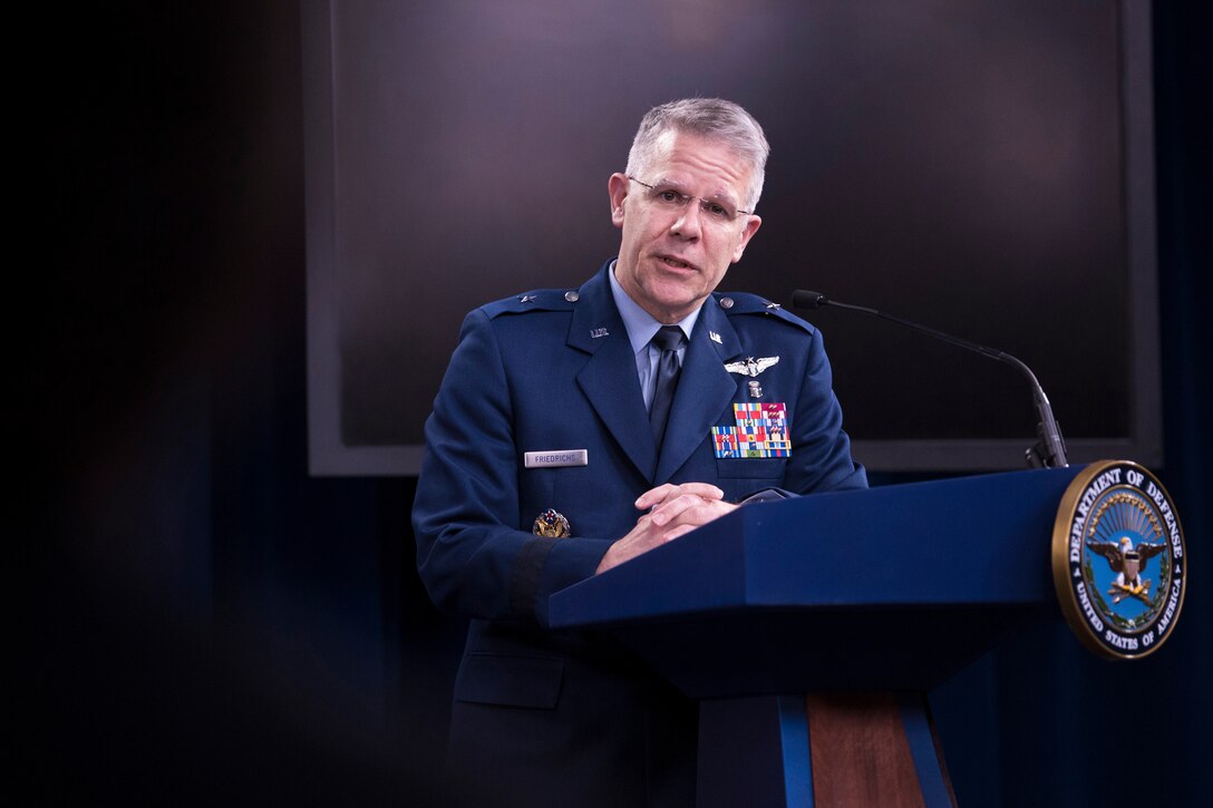 A military officer stands behind a dias and speaks.