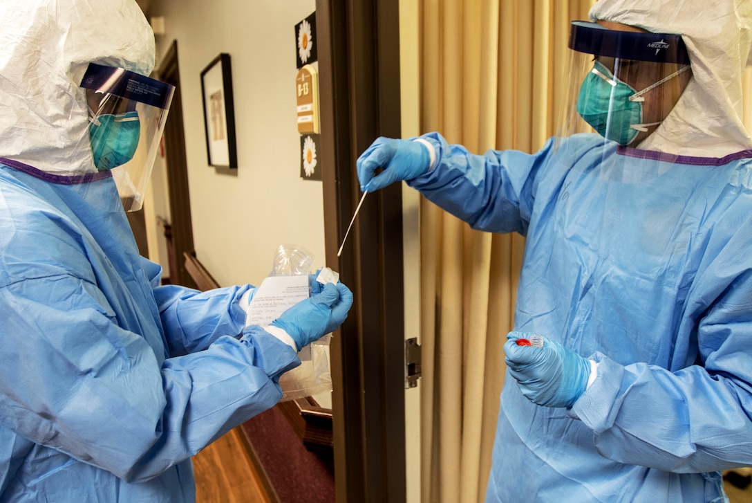 Two people dressed in personal protective equipment test a nasal swab.