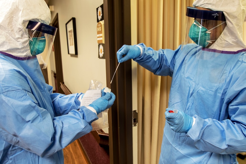 Two people dressed in personal protective equipment test a nasal swab.