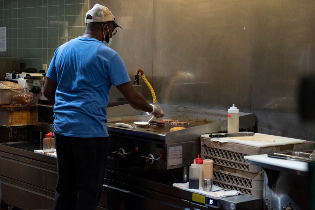 A photo of a worker grilling hamburgers.