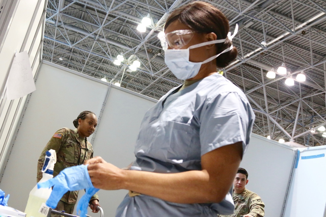 A woman in hospital scrubs puts on rubber gloves.
