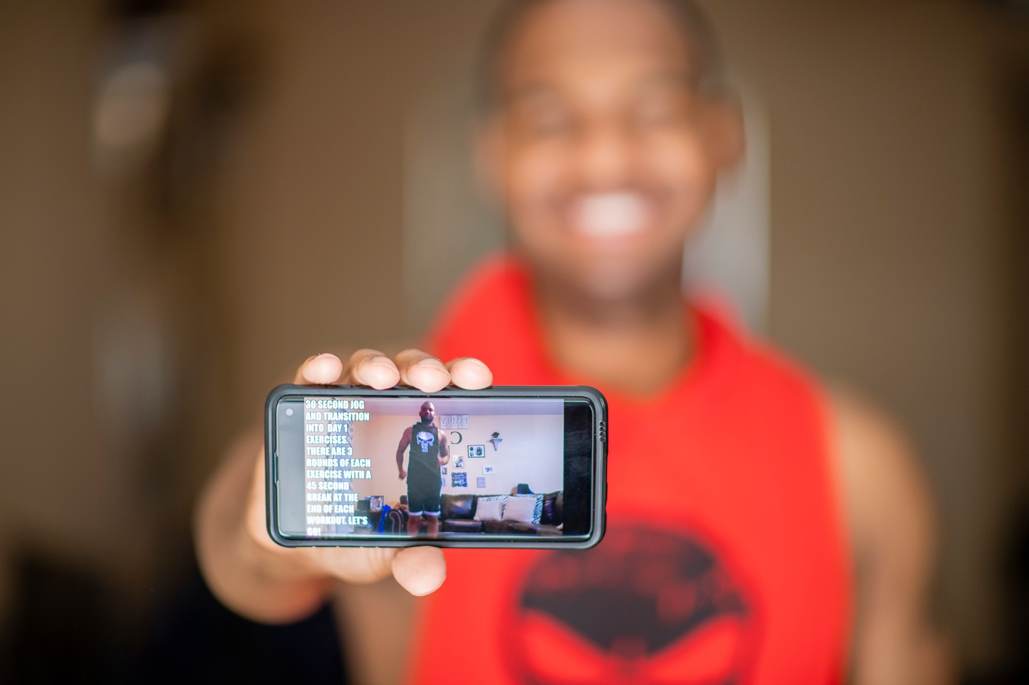 Staff Sgt. Kevin holds out his phone for the camera creating a shallow depth of field photo with the phone in focus but everything else is blurry.