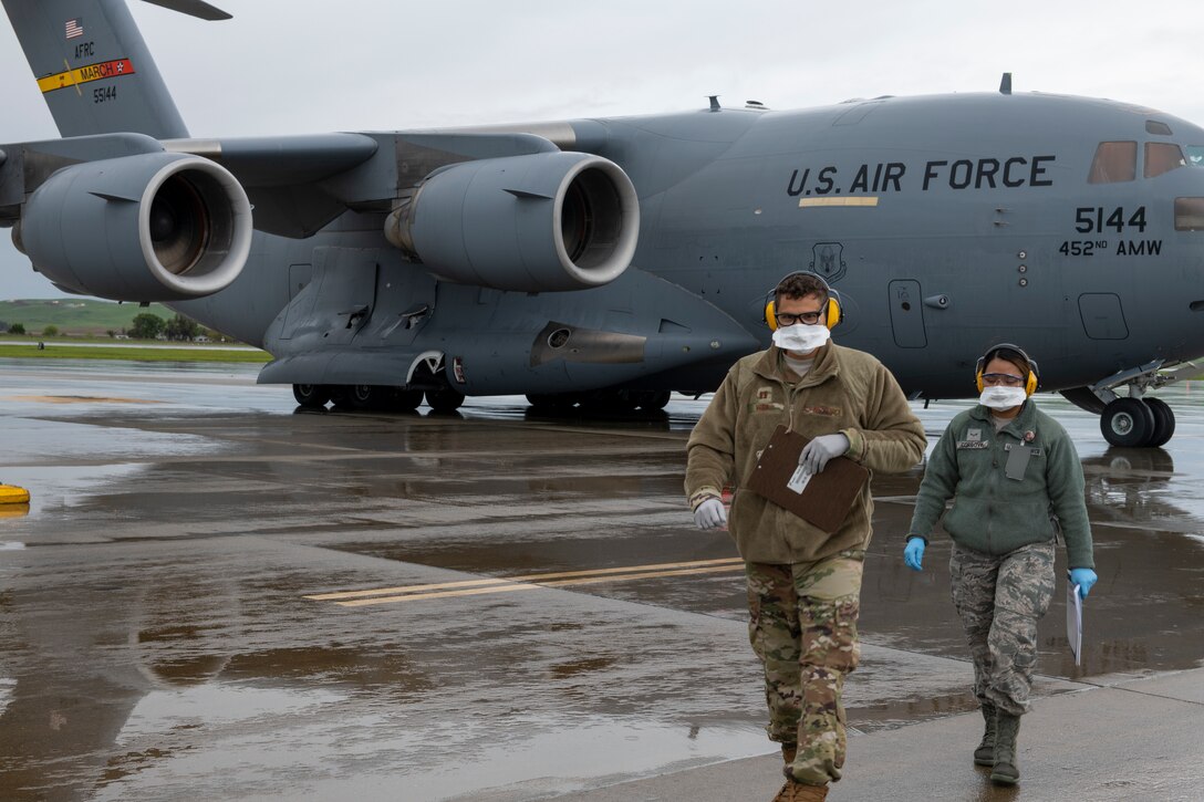 Two airmen wearing protective masks walk away from a large transport jet.