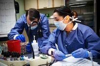 Two Navy medical technicians in personal protective equipment handle vials in a laboratory.