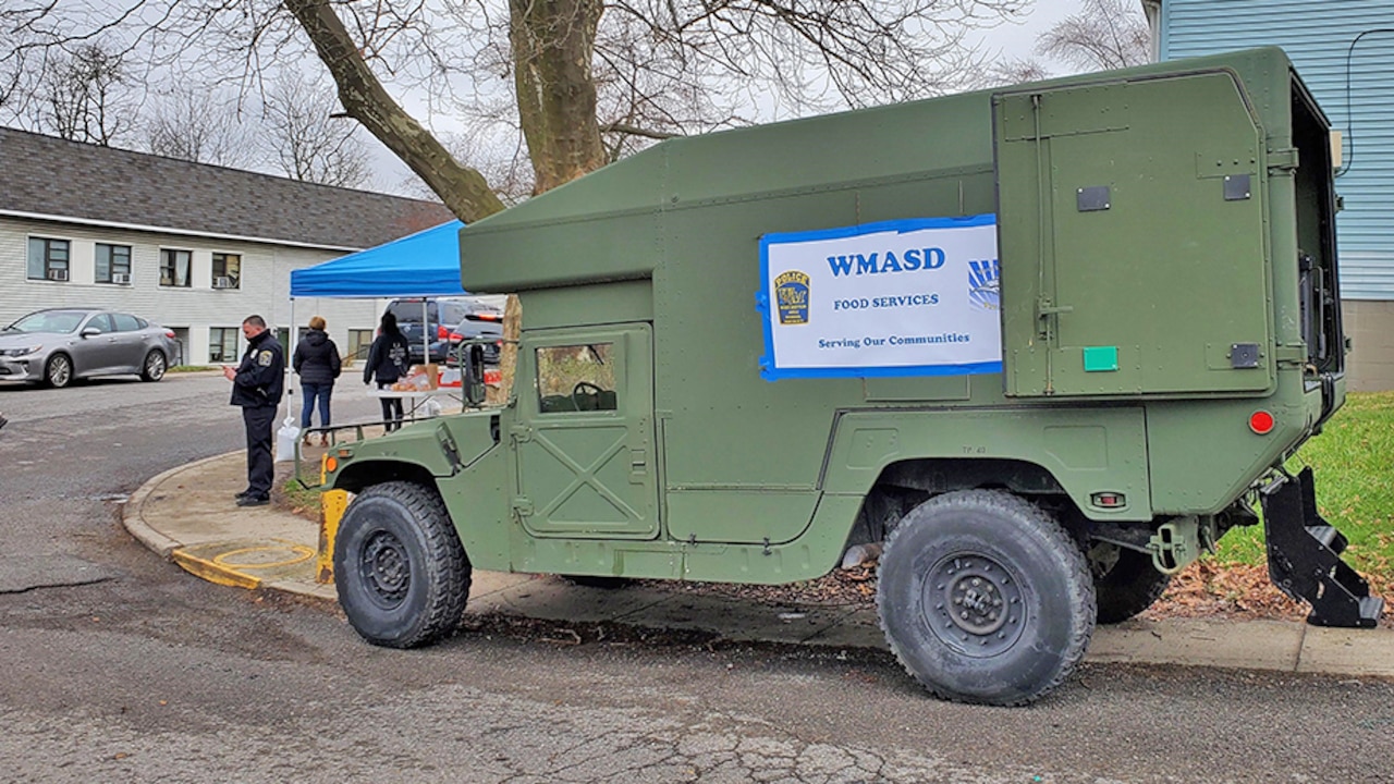 A parked former military vehicle carries a sign that it is being used as a food service truck.