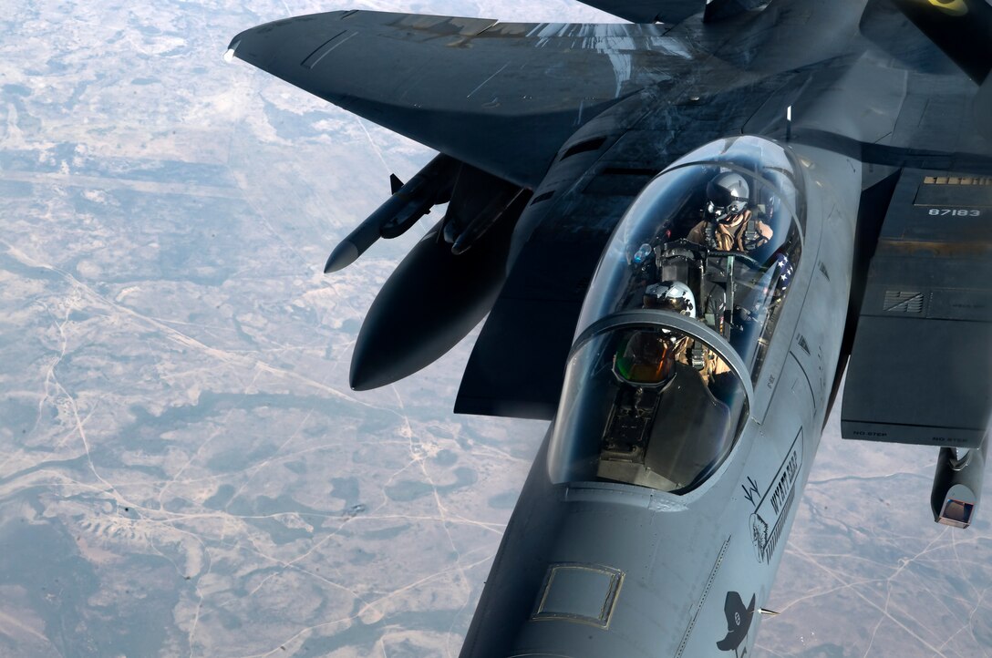 Two airmen are visible in the cocket of an in-flight fighter jet.