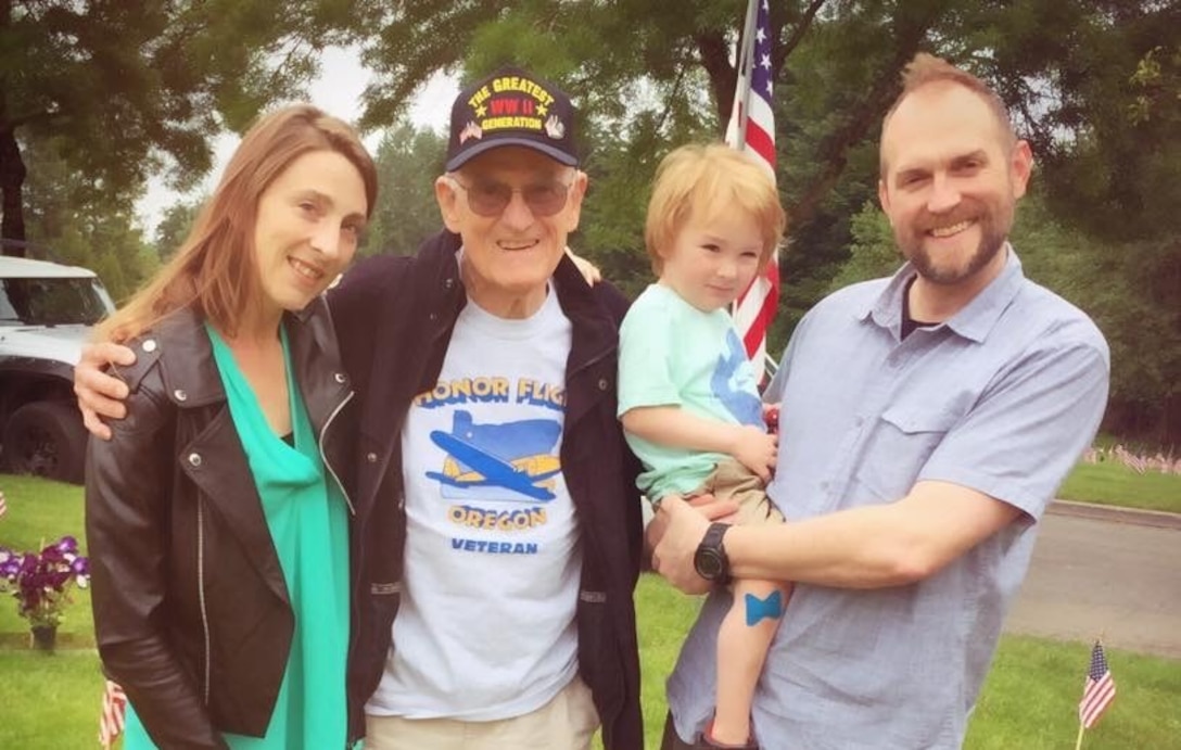 A man, woman,  and a little boy pose for a photo with an elderly man wearing a World War II veterans cap.