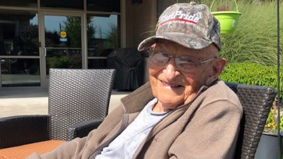 An elderly man wearing a ballcap smiles.