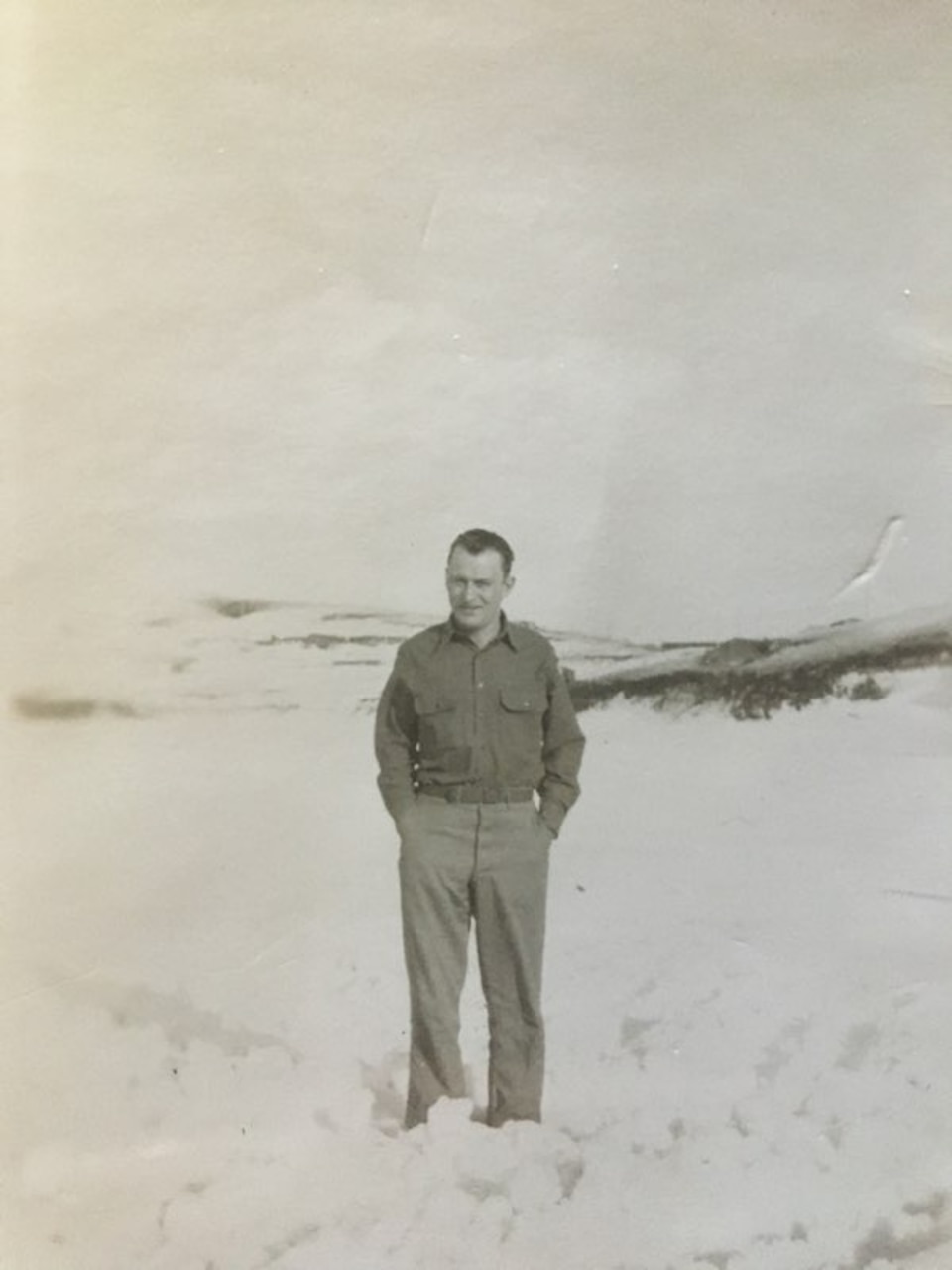 A man in an Army uniform stands outside in the snow.