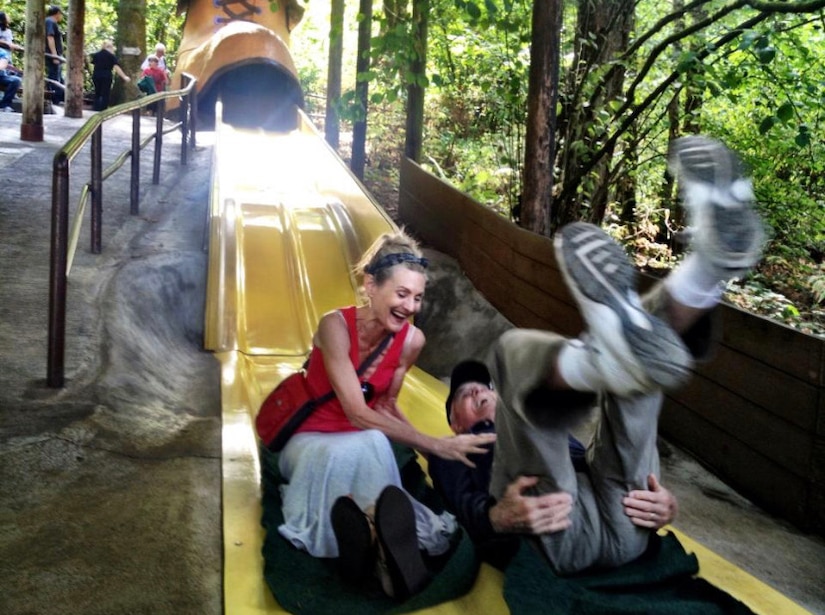 A woman and an elderly man laugh after sliding down a large, two-person slide.