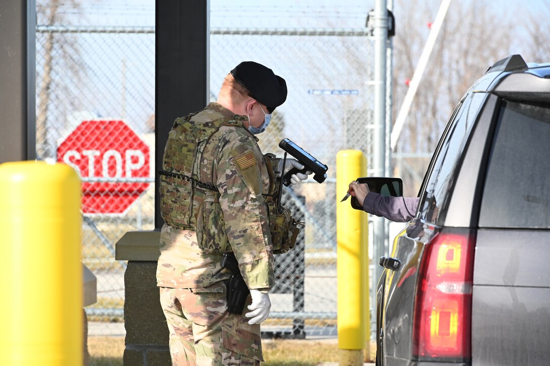 Photo of 119th Security Forces Airman checking identification for entry at the North Dakota Air National Guard Base, Fargo, N.D., April 8, 2020, as he wears personal protective equipment to prevent the spread of the Novel Coronavirus.