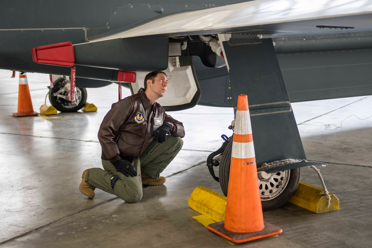 Officer in green flight suit looks under an aircraft wing.