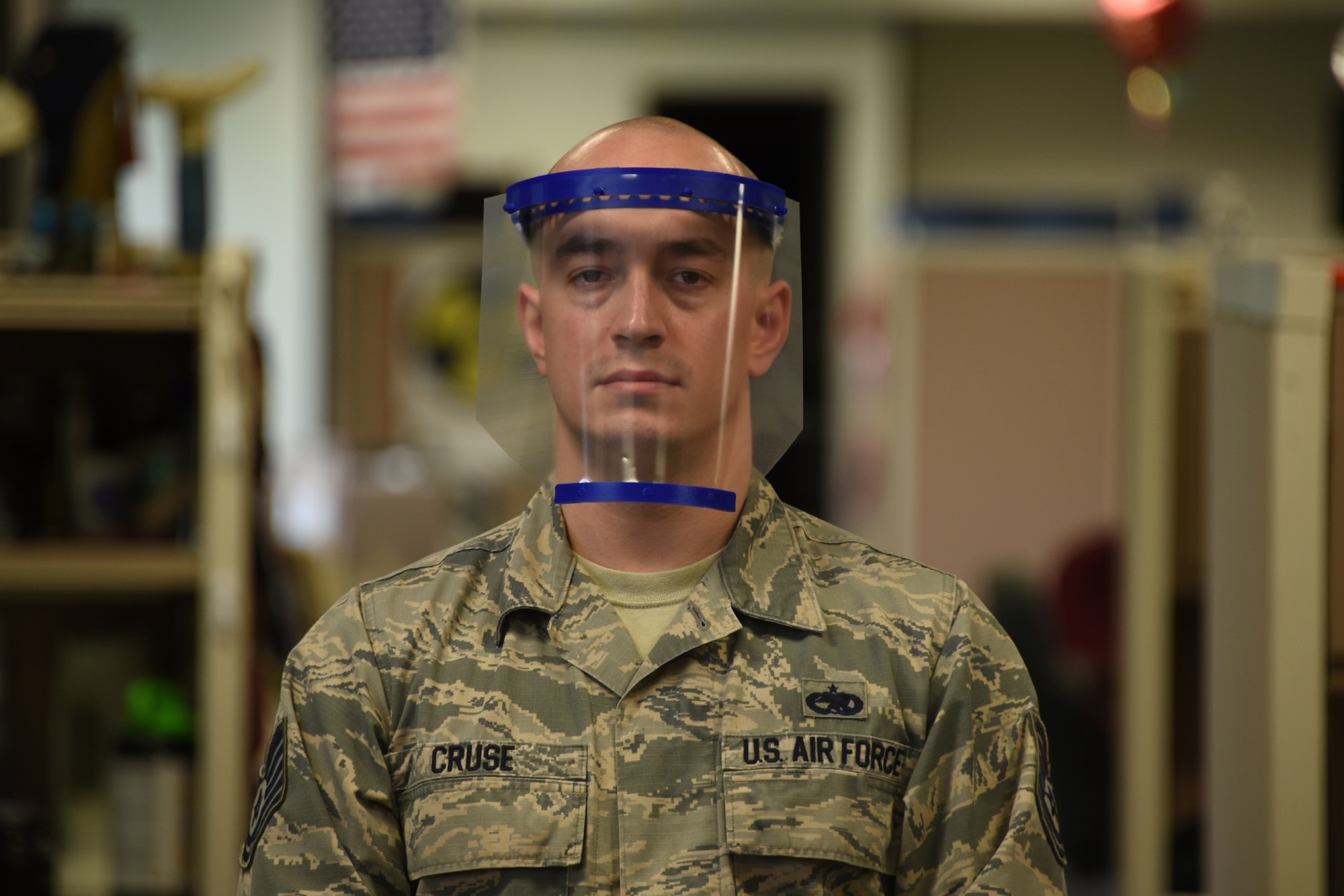Tech. Sgt. Joel Cruse, 363rd Training Squadron AMMO instructor, demonstrates how the face shield he made from a 3D printer and a few other items is properly worn at Sheppard Air Force Base, Texas, April 7, 2020. Face shields are a clear physical barrier for liquid droplets. If someone who is symptomatic coughs near or in the direction of the face of someone where the shield, it prevents those droplets from reaching facial points of entry. (U.S. Air Force photo by Staff Sgt. Robert L. McIlrath)