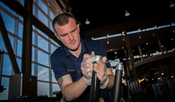 Airman cleans work-out machine in gym.