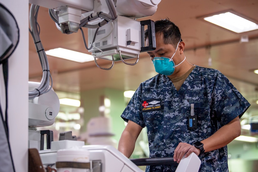 A service member wearing a paper face mask operates a piece of medical equipment.