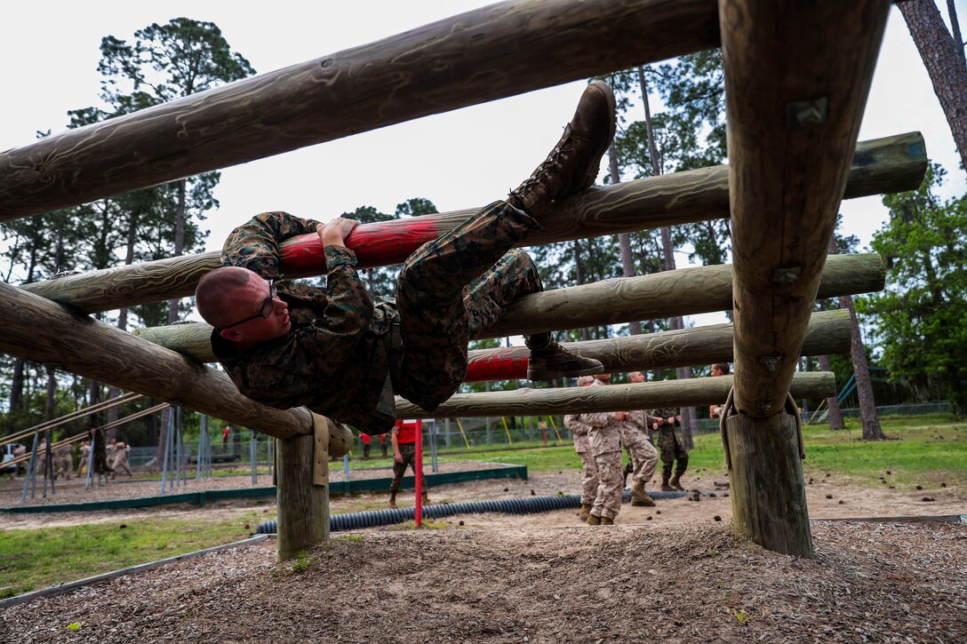 A man hangs in the air while holding on to a log obstacle.