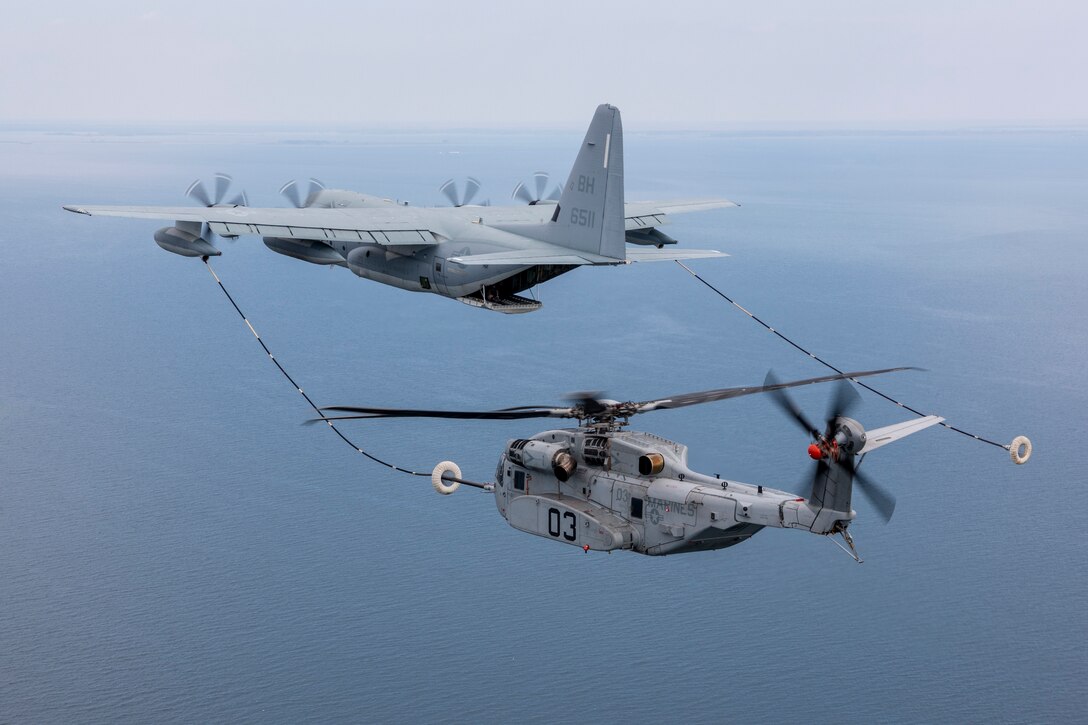 An aircraft flies in front of a helicopter above open water.